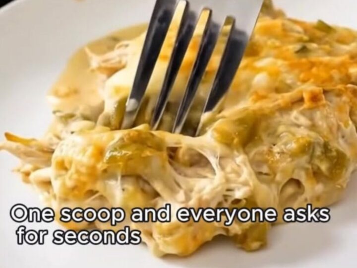 A spatula lifting a portion of creamy green chile chicken enchilada casserole from a glass dish.