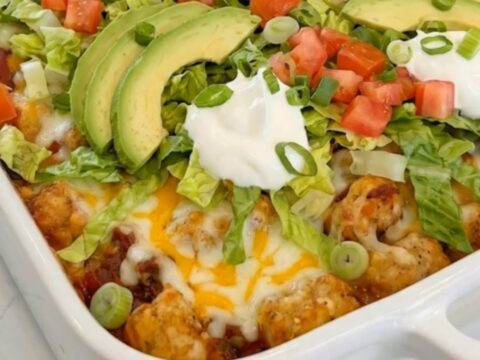 A steaming cheesy taco tater tot casserole in a rectangular ceramic dish.