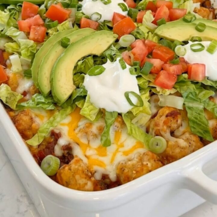 A steaming cheesy taco tater tot casserole in a rectangular ceramic dish.