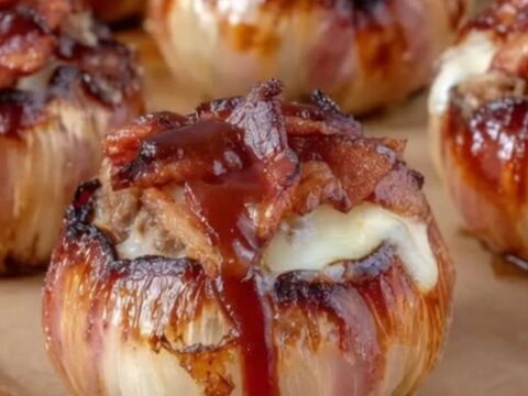 Glistening barbecue glazed onion bombs wrapped in crispy bacon resting on parchment paper
