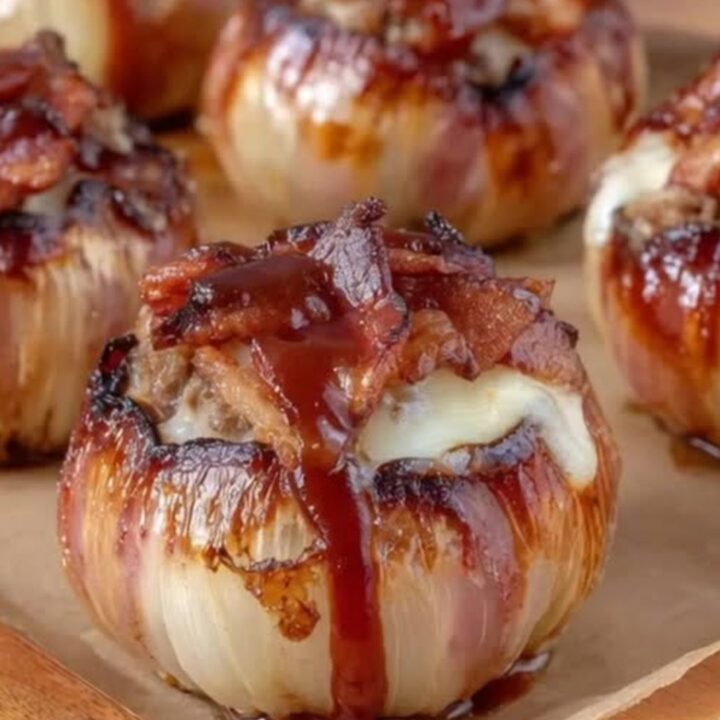 Glistening barbecue glazed onion bombs wrapped in crispy bacon resting on parchment paper
