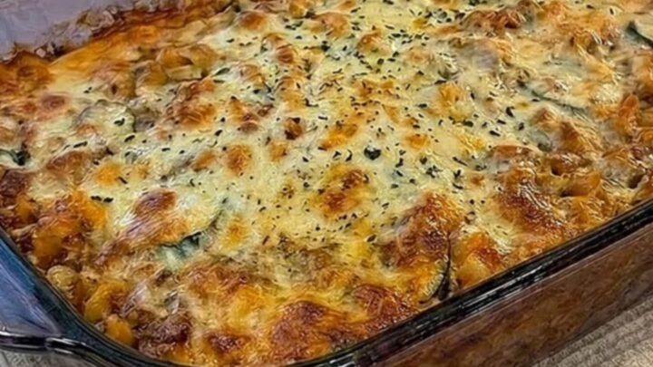 A clear glass dish filled with a bubbly, golden-brown pasta bake on a kitchen counter.