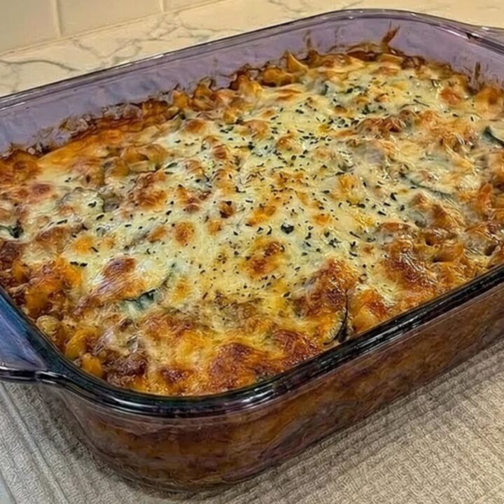 A clear glass dish filled with a bubbly, golden-brown pasta bake on a kitchen counter.