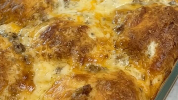 A bubbly, cheesy breakfast biscuit casserole in a 9x13 dish with a long cheese pull.