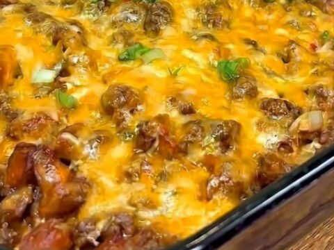 A close-up of a chili cheese dog casserole in a glass dish with a long, stretchy cheese pull.