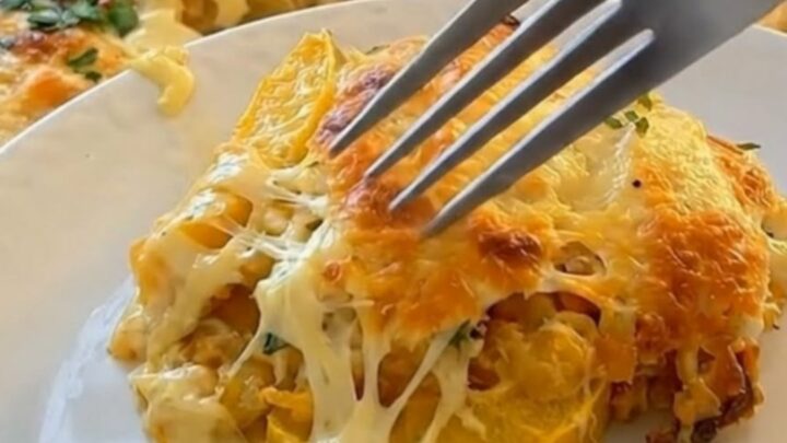 A golden-brown baked yellow squash casserole in a glass dish with a piece being scooped out.