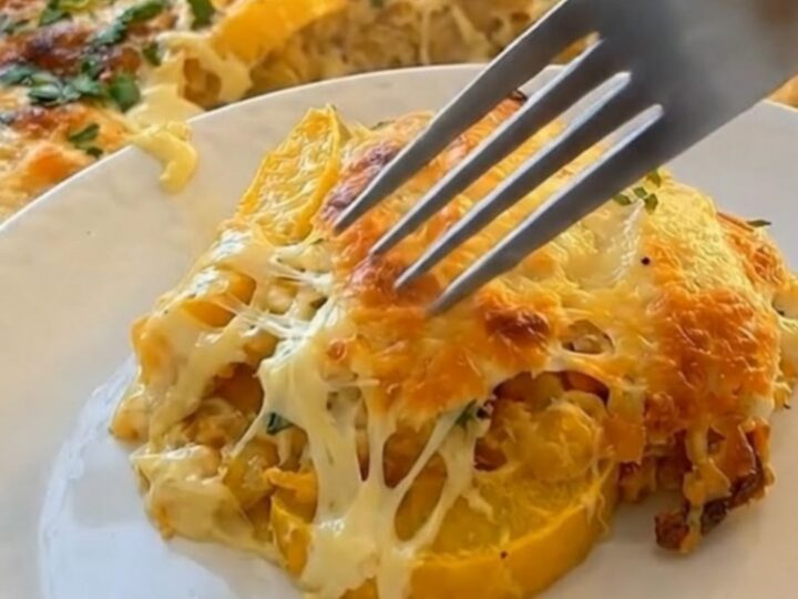 A golden-brown baked yellow squash casserole in a glass dish with a piece being scooped out.