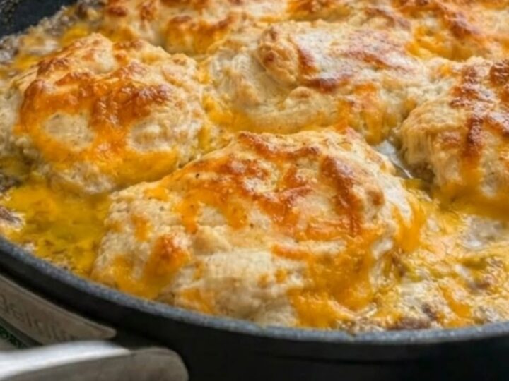 A golden, bubbly cheddar bay hamburger casserole in a black skillet with a spatula lifting a serving.