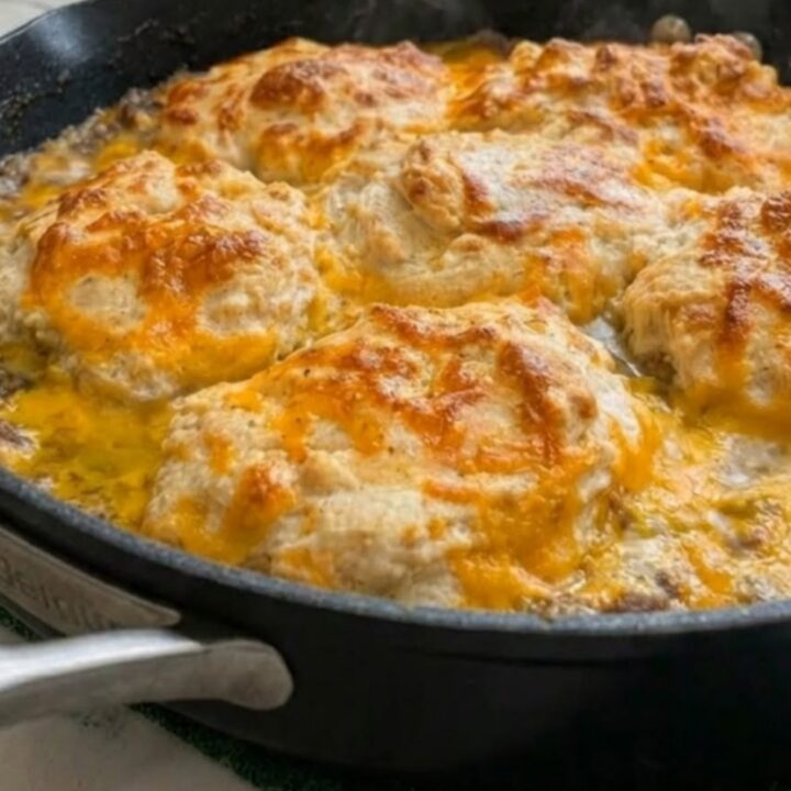 A golden, bubbly cheddar bay hamburger casserole in a black skillet with a spatula lifting a serving.