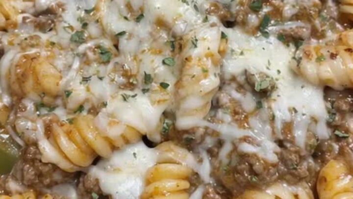 A rustic cast iron skillet filled with cheesy rotini pasta and ground beef topped with melted provolone cheese and dried