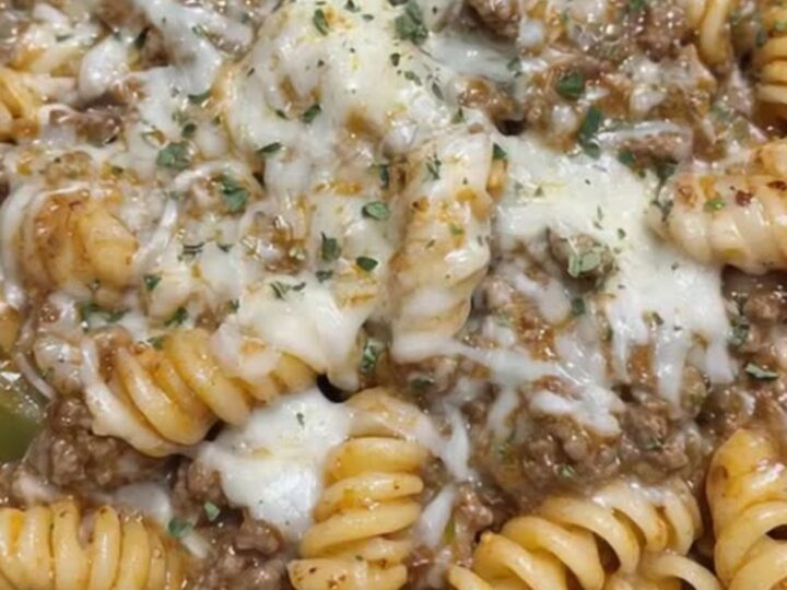 A rustic cast iron skillet filled with cheesy rotini pasta and ground beef topped with melted provolone cheese and dried