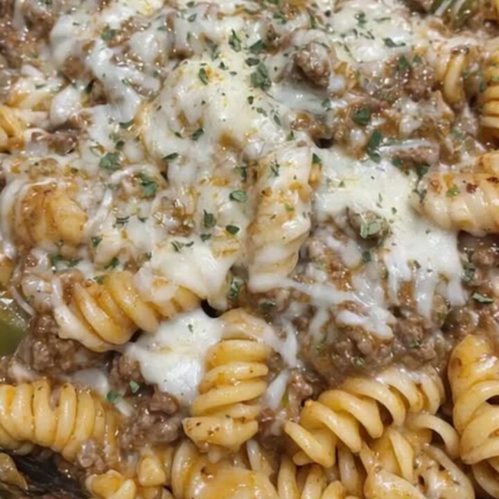 A rustic cast iron skillet filled with cheesy rotini pasta and ground beef topped with melted provolone cheese and dried