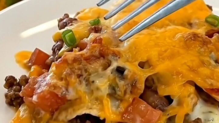 A steaming, cheesy beef and tortilla casserole in a blue baking dish on a kitchen counter.