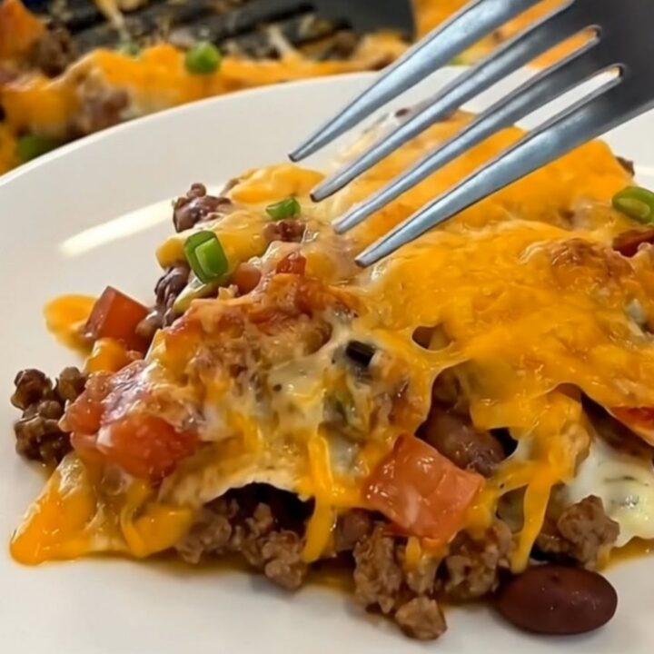 A steaming, cheesy beef and tortilla casserole in a blue baking dish on a kitchen counter.