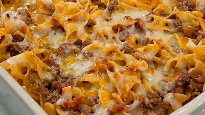 A steaming cheesy ground beef noodle casserole in a grey ceramic dish.