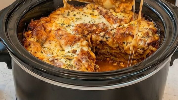 A golden-brown slow cooker lasagna with melted cheese pulls being lifted from the pot.