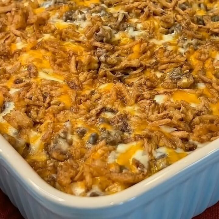 A bubbly, cheesy French onion hamburger casserole in a white fluted ceramic dish.