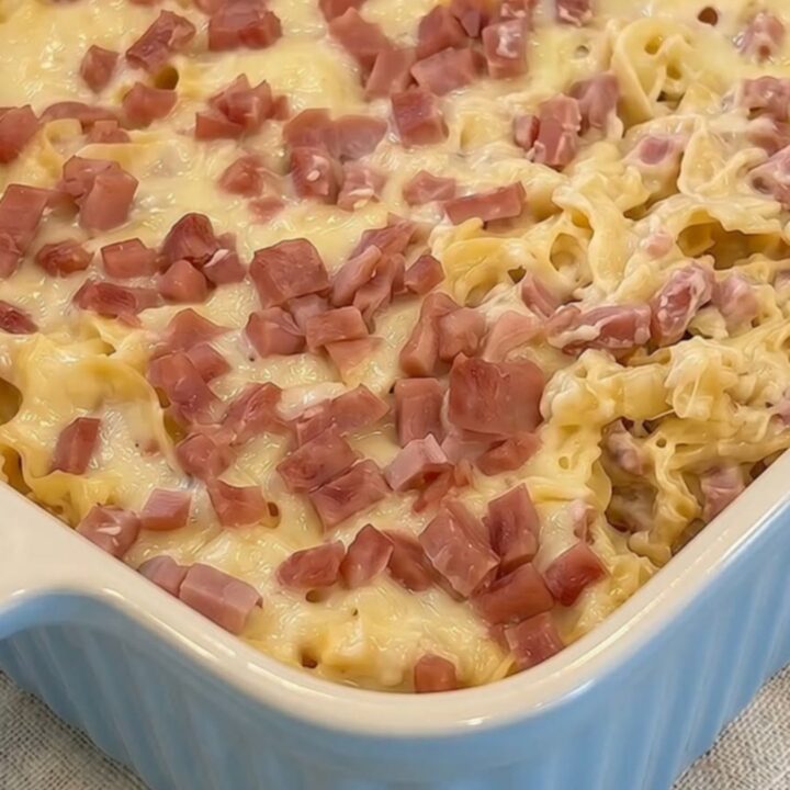 A steaming, creamy Swiss ham and noodle casserole in a fluted baking dish.