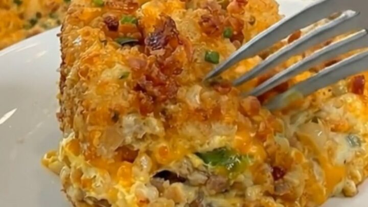 A golden, cheesy breakfast casserole in a glass dish topped with crispy tater tots and bacon.