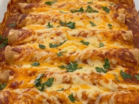 Cheesy ground beef enchiladas baked in a white ceramic dish topped with red sauce, cheese, and cilantro.
