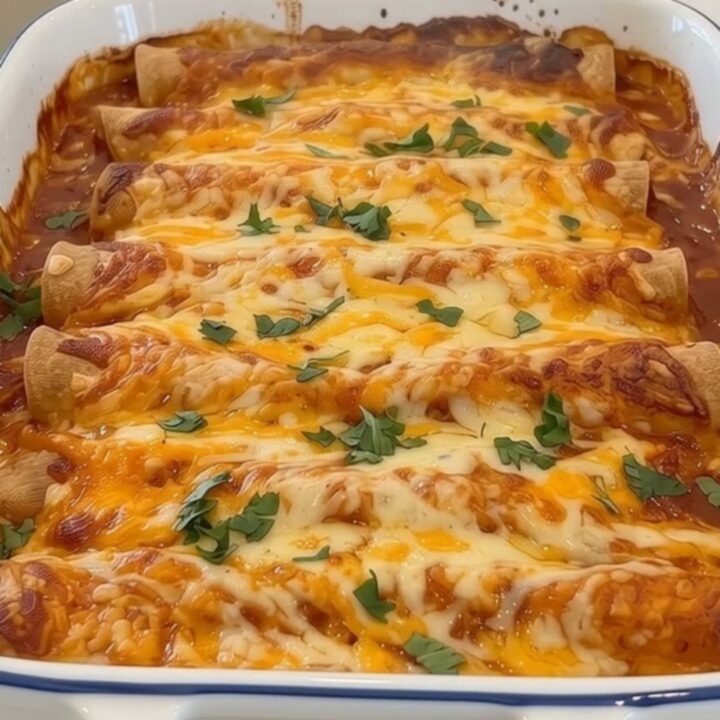 Cheesy ground beef enchiladas baked in a white ceramic dish topped with red sauce, cheese, and cilantro.