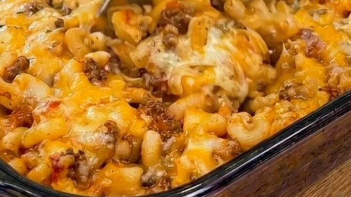 A glass baking dish filled with golden, cheesy Johnny Marzetti casserole under warm kitchen lighting.