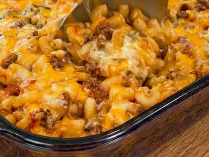 A glass baking dish filled with golden, cheesy Johnny Marzetti casserole under warm kitchen lighting.