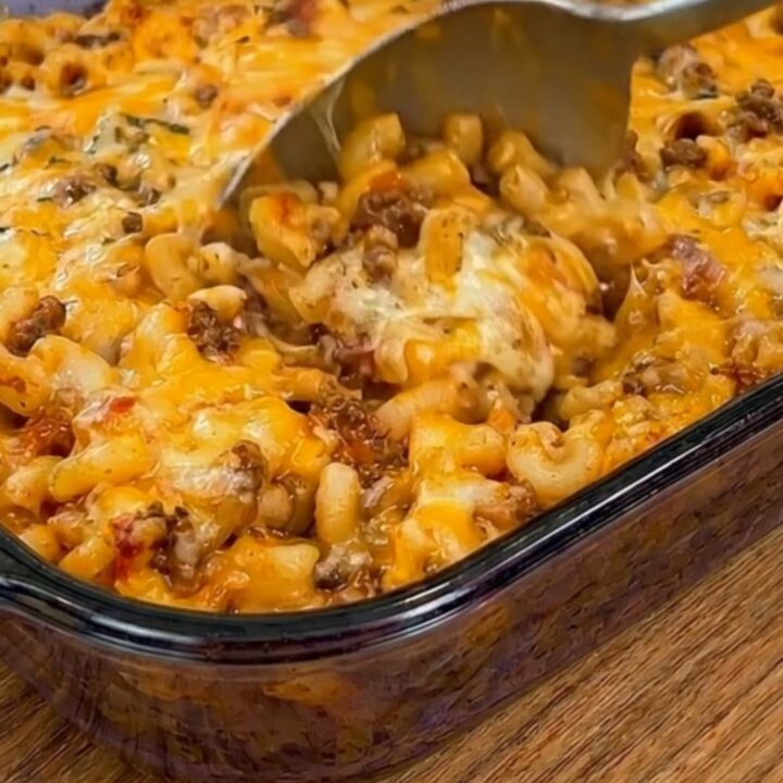 A glass baking dish filled with golden, cheesy Johnny Marzetti casserole under warm kitchen lighting.