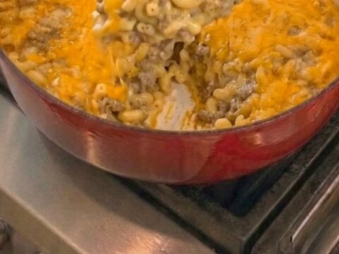 A close-up view of a red cast-iron skillet filled with cheesy macaroni and ground beef.
