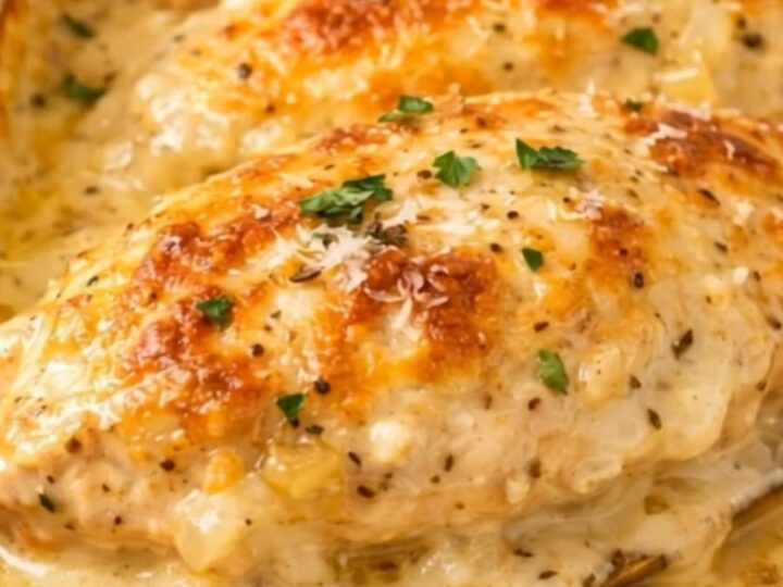 A golden, cheese-crusted chicken breast in a white baking dish with rising steam.