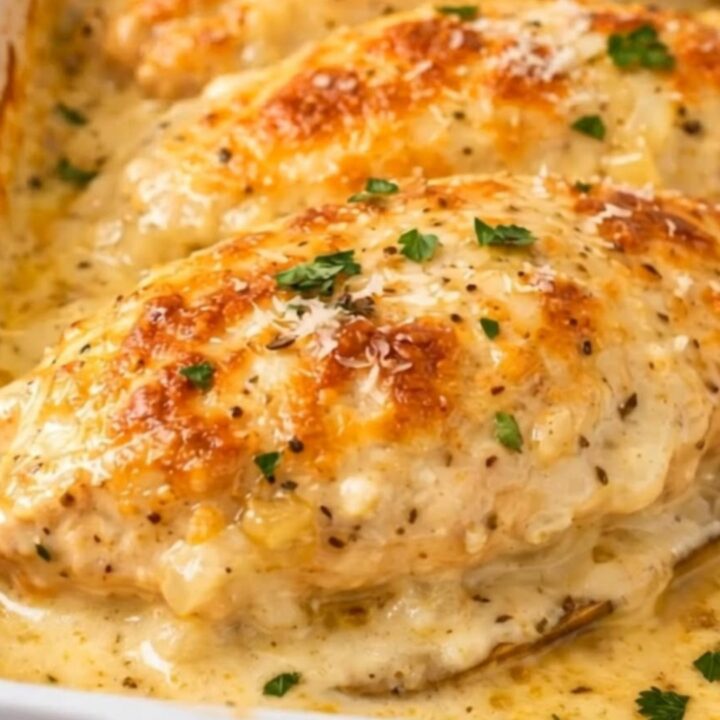 A golden, cheese-crusted chicken breast in a white baking dish with rising steam.