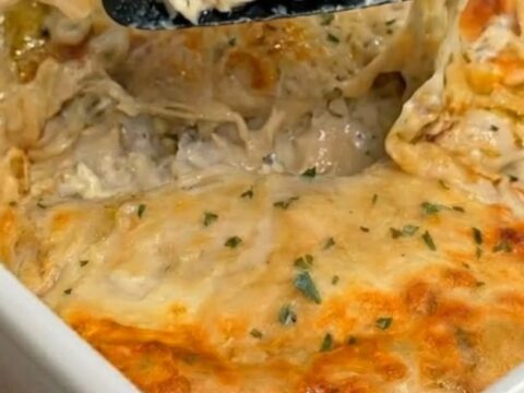 A cheesy, sauce-drenched creamy white chicken enchilada portion being lifted from a white baking dish.