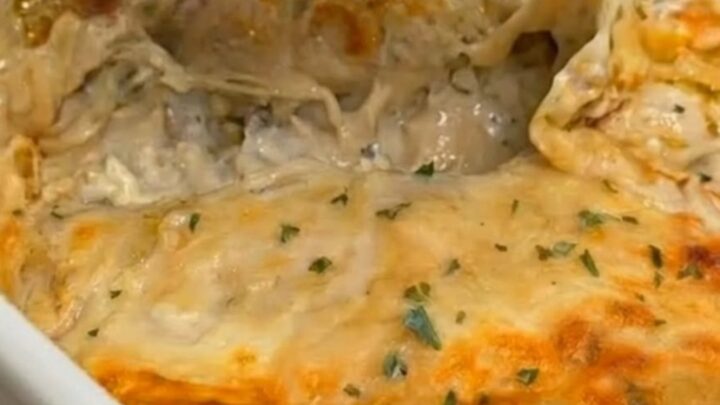 A cheesy, sauce-drenched creamy white chicken enchilada portion being lifted from a white baking dish.