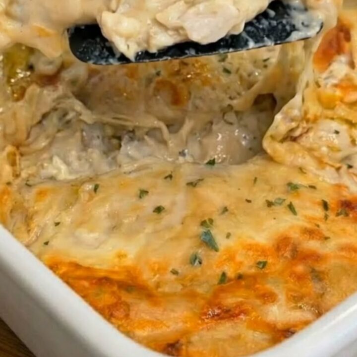 A cheesy, sauce-drenched creamy white chicken enchilada portion being lifted from a white baking dish.