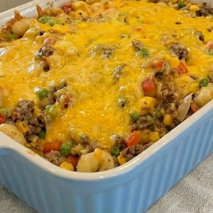 A steaming scoop of Shipwreck Casserole being lifted from a light blue ceramic dish with melted cheddar cheese.