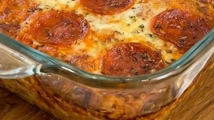 A warm square of pepperoni pizza bake being lifted from a glass dish with a metal spatula.