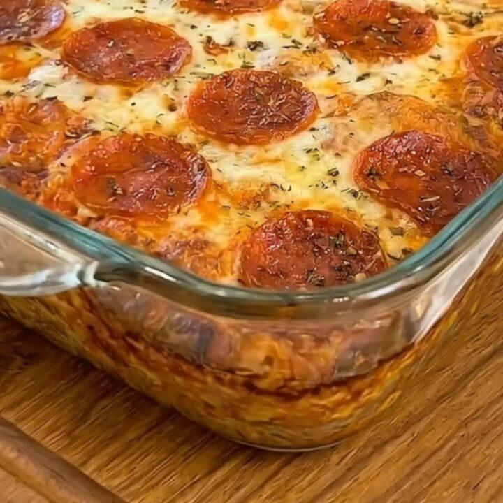 A warm square of pepperoni pizza bake being lifted from a glass dish with a metal spatula.