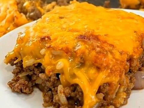 A steaming square portion of Tex-Mex beef casserole with a gooey melted cheese pull being lifted from a white baking dish.