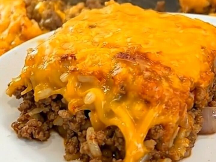 A steaming square portion of Tex-Mex beef casserole with a gooey melted cheese pull being lifted from a white baking dish.