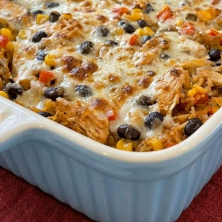 A cheesy chicken burrito casserole in a blue fluted baking dish, showing melted cheese and visible chicken and beans.