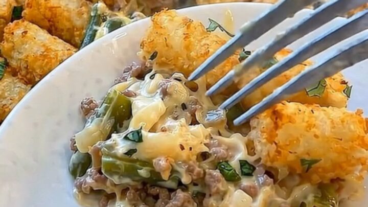 A metal spatula lifting a scoop of cheesy green bean tater tot casserole from a glass baking dish.