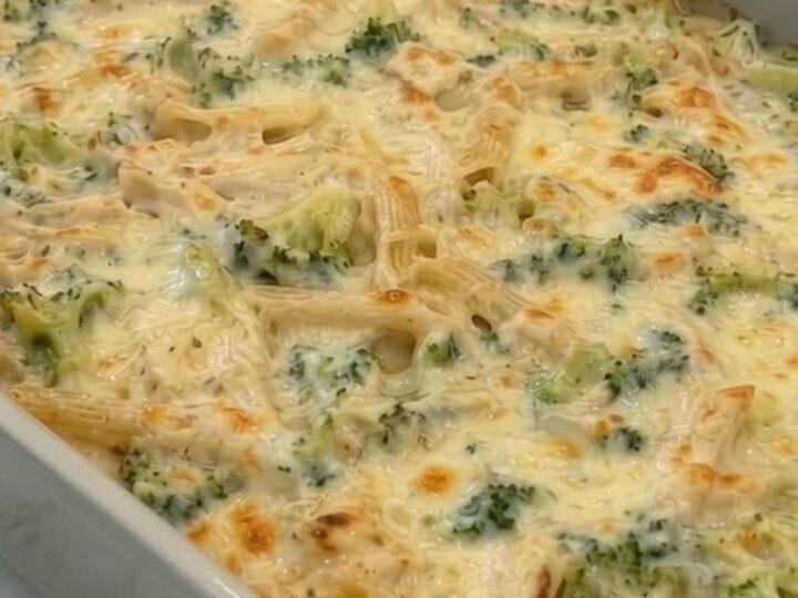 A golden, bubbling chicken alfredo pasta bake in a ceramic dish, showing a long cheese pull with steam.