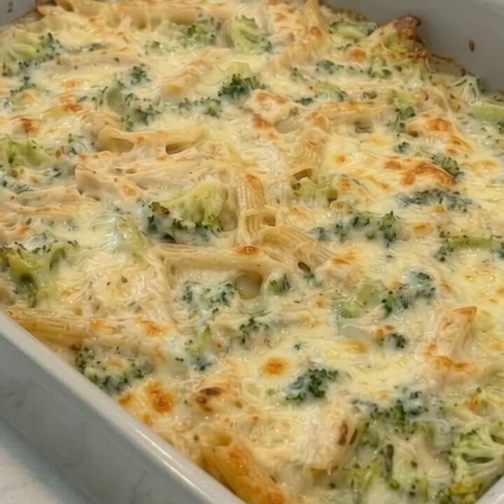 A golden, bubbling chicken alfredo pasta bake in a ceramic dish, showing a long cheese pull with steam.
