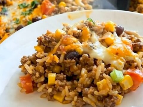 A steaming portion of Mexican rice casserole with black beans, corn, and melted cheese in a stainless steel skillet.