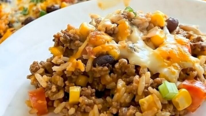 A steaming portion of Mexican rice casserole with black beans, corn, and melted cheese in a stainless steel skillet.