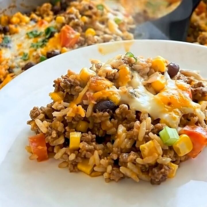 A steaming portion of Mexican rice casserole with black beans, corn, and melted cheese in a stainless steel skillet.