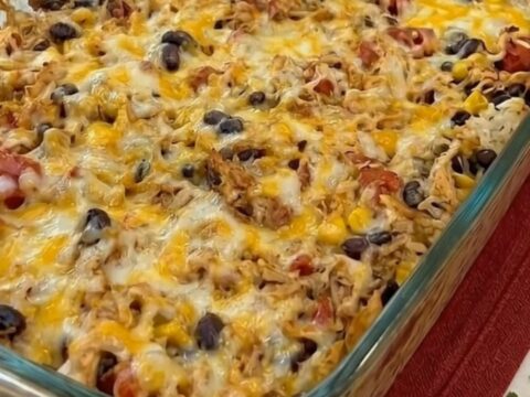 A steaming glass baking dish filled with a cheesy chicken and rice burrito casserole.