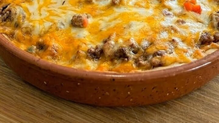 A warm, bubbly burrito pie in a terracotta dish with a long, golden cheese pull being lifted by a pie server.