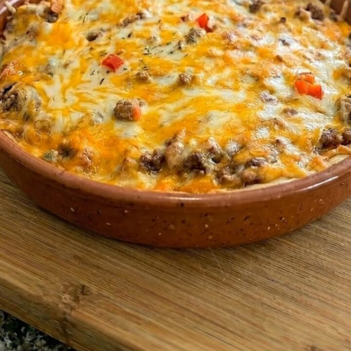 A warm, bubbly burrito pie in a terracotta dish with a long, golden cheese pull being lifted by a pie server.