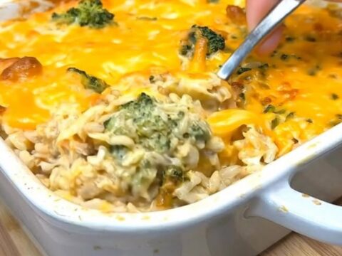 A steaming, cheesy chicken broccoli rice casserole in a white baking dish.